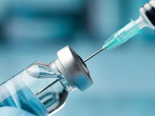 Close-up of a syringe needle piercing the rubber stopper of a clear medicine vial against a cool blue background, suggesting a clinical vaccination setting.