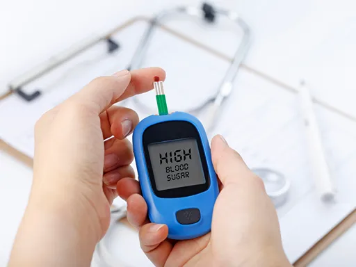 Hands hold a blue blood sugar meter displaying “HIGH”, with a test strip inserted; a stethoscope and clipboard sit blurred in the background, suggesting concern.